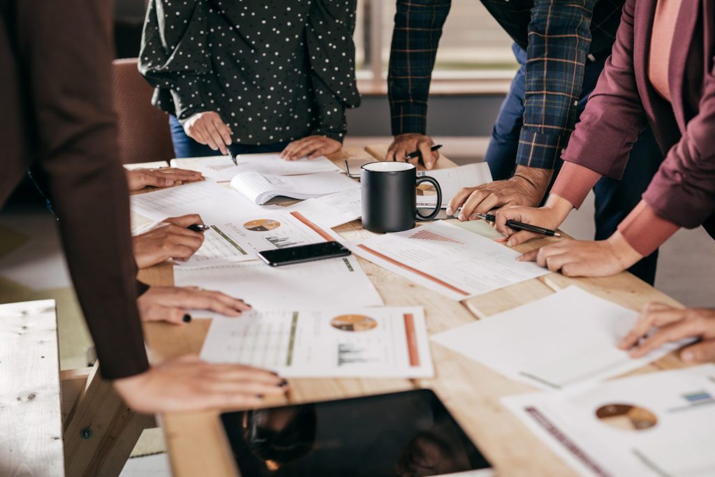 Group of people over a table with reports. Demonstrating the concept of brainstorming or discussion regarding financial impact of COVID on Healthcare ecosystems.