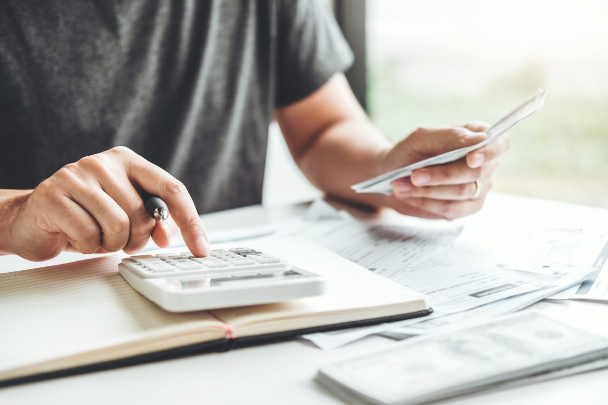 Person using calculator and holding receipts. There are various bills and cheques around. Meant to represent how provider relief fund can help providers during COVID.