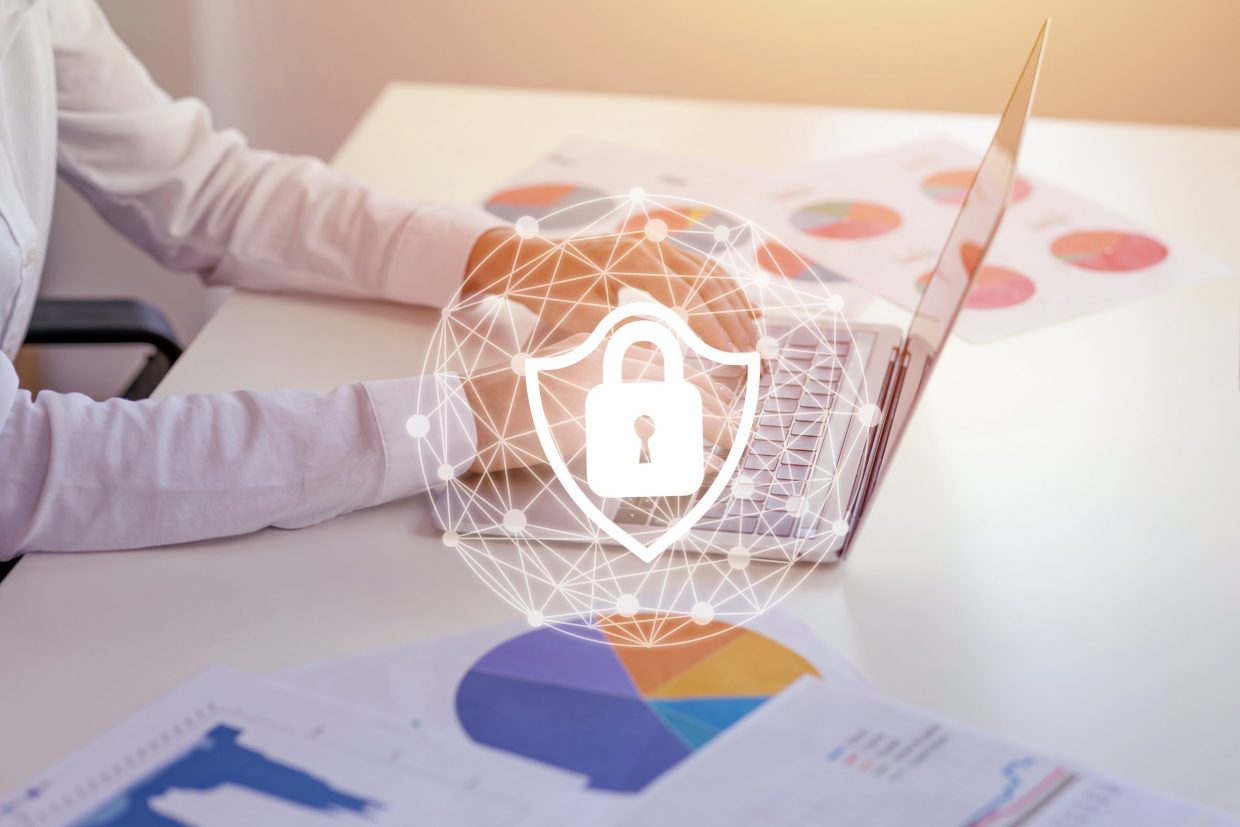 Person working on a laptop with an overlap image of a security circle with a padlock on a shield to represent security.